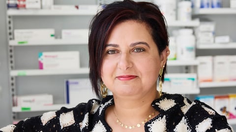 Pharmacist Noha El Sayed standing in front of a wall of prescription medications