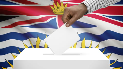 A ballot box with a hand is seen in front of the B.C. flag.