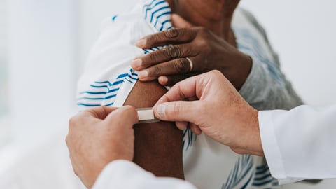 Pair of hands sticking a bandage over flu shot area on woman's shoulder