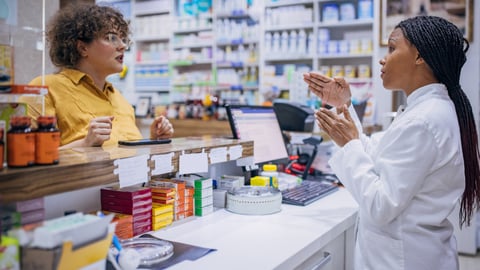 Two dark skinned women having a conversation inside a pharmacy