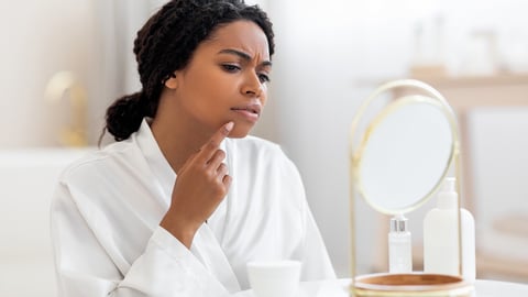 Dark-skinned woman touching her acne as she looks in the mirror