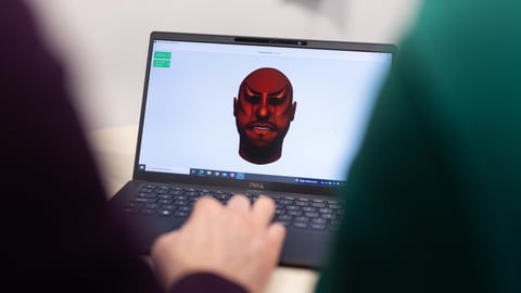 A person looks at a laptop computer where on the screen is an angry red face.