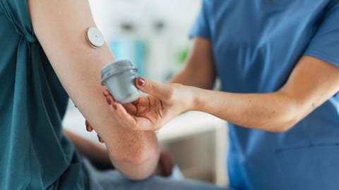 A woman with a continuous glucose monitor in her arm and a pharmacist helping her with it