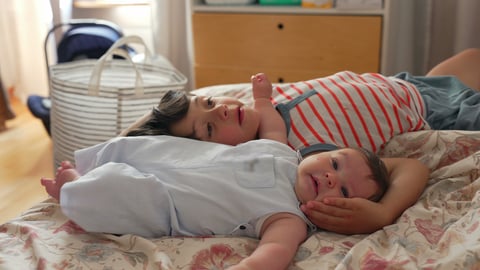 White boy and baby lying on bed, boy cradling baby's head