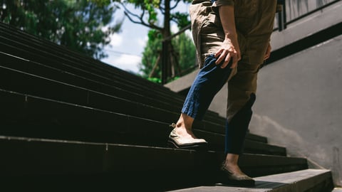 Older woman clutching her knee in pain going down outdoor stairs