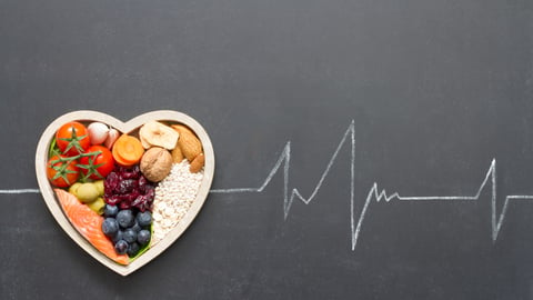 heart-shaped bowl of healthy produce on backdrop of heartbeat ECG graph.