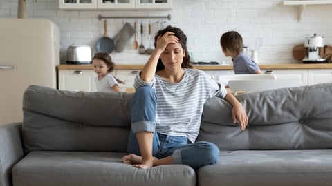 Young tired single mother suffers from headache closed eyes touch forehead sitting on couch while her daughter and son running around her and shouting, female babysitter feels exhausted by noisy kids; Shutterstock ID 1606546576