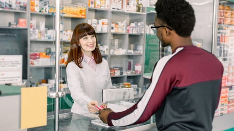 Young woman pharmacist giving medications to the male African client standing at the paydesk of the pharmacy store; Shutterstock ID 1457864657