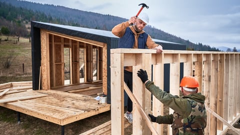 Man worker building wooden frame house on pile foundation. Carpenter hammering nail into wooden joist, using hammer. Carpentry concept.; Shutterstock ID 2356031675