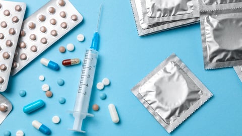 Birth control pills, an injection syringe and condom in a package on blue background. The concept of choosing method of contraception, birth control pills or condom.; Shutterstock ID 1266659281