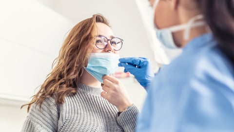 Smiling girl puts face mask off her nose so that a healthcare worker can take a sample for Covid-19 testing.; Shutterstock ID 1934424008