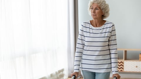 Thoughtful sad disabled injured old woman standing alone holding walking frame at home, depressed lonely handicapped senior grandmother look through window using walker, elder people physiotherapy; Shutterstock ID 1562124112