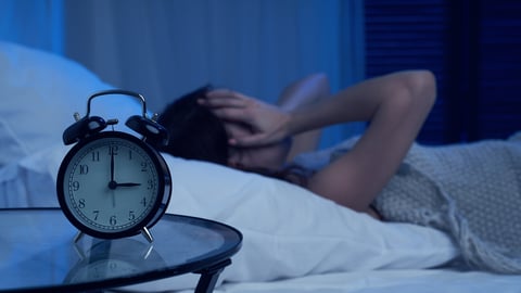 Unhappy woman with insomnia lying on bed next to alarm clock at night; Shutterstock ID 1706492998