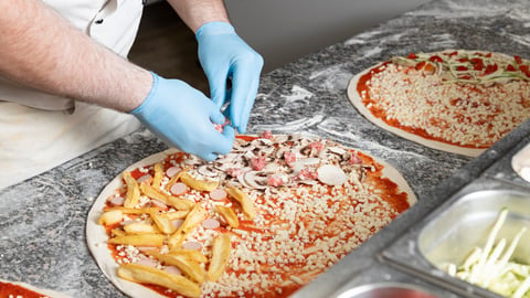 Pizzaiolo puts ingredients on a fresh pizza. Cooking pizza during time of Covid 19. Hands of the chef with sterile gloves.; Shutterstock ID 1745366228