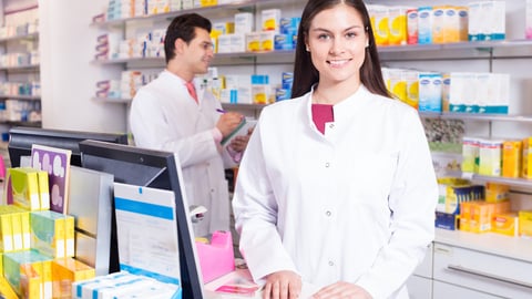 Cheerful pharmacist standing at pay desk and pharmacy technician helping ; Shutterstock ID 344514917