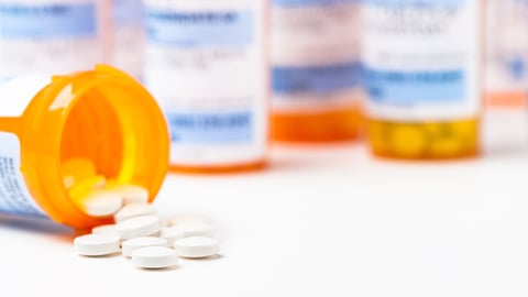 Round white prescription medication medicine pill tablets spilling from a bottle with numerous full bottles in background.; Shutterstock ID 498009256