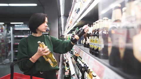 A beautiful girl takes alcoholic drinks from the supermarket shelf. Shopping for alcohol in the store. The girl chooses a drink in the supermarket.; Shutterstock ID 778046629