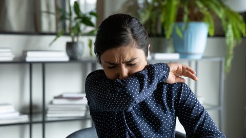 Millennial indian ethnic girl sitting in office, coughing in elbow, right illness behavior for not spreading virus infection. Unhealthy young woman feeling unwell at workplace, covid 19 symptoms.; Shutterstock ID 1694217865