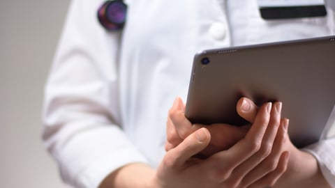 Tablet in the hands of healthcare professional up close. White coat, stethoscope, and badge visible in background. Hands of nurse practitioner or PA using technology in medicine for patients; Shutterstock ID 1709407906