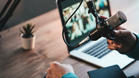 A man host streaming his audio podcast using microphone and laptop at his small broadcast studio, close-up; Shutterstock ID 1931610278