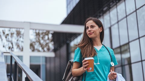 Smiling female surgeon standing outdoors while looking away. A female healthcare worker leaving the hospital in her uniform. Representation of the daily life of a nurse going to work; Shutterstock ID 2386565033