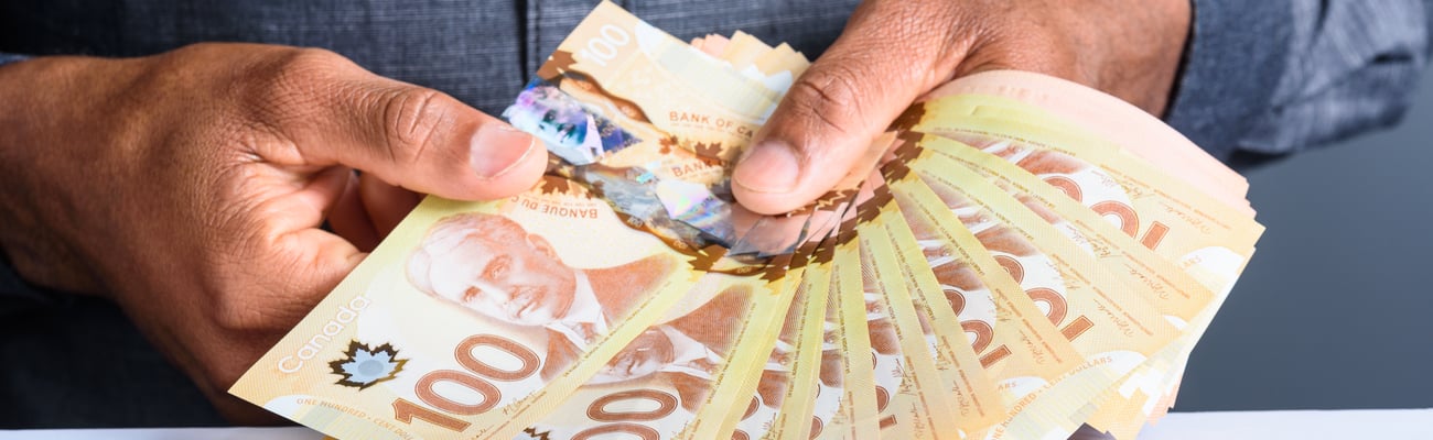 Hand holding many Canadian one-hundred dollar bills