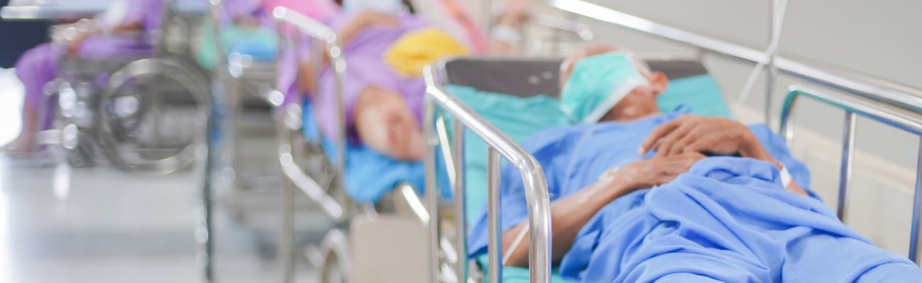 People lying in a row on stretchers in a crowded hospital