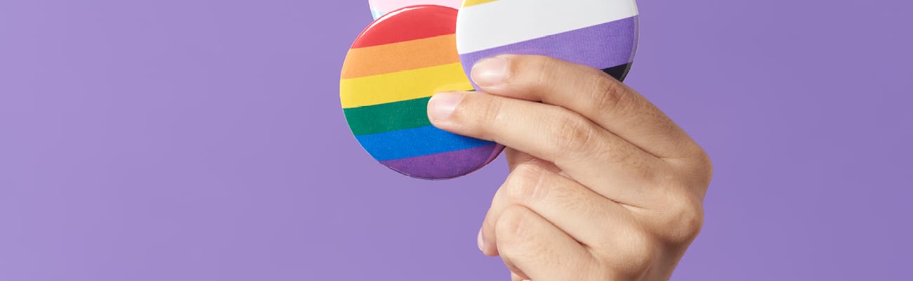 White hand holding up buttons denoting different pride flags