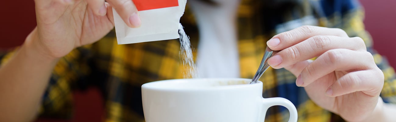 Close up of a young person pouring a packet of sugar substitute into a cup of coffee