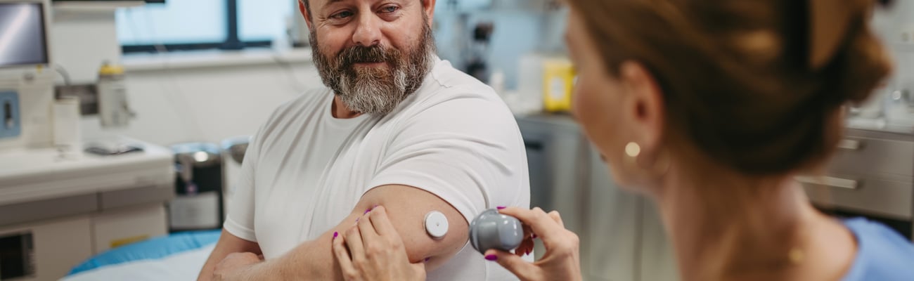 Doctor applying a continuous glucose monitor sensor on patient's arm.