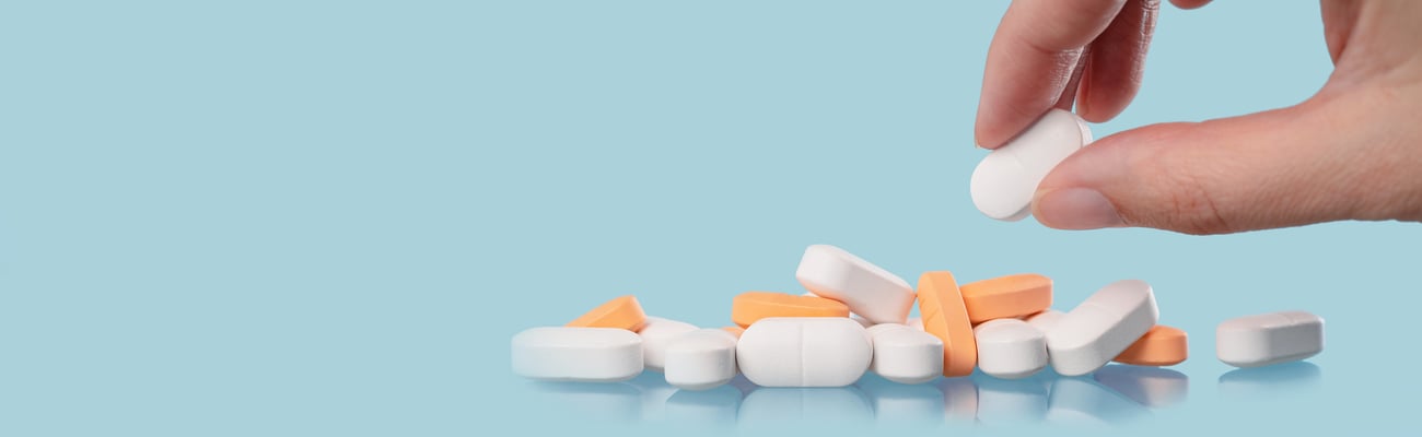 opioid pills or other pills on blue background, white hand selecting a pill