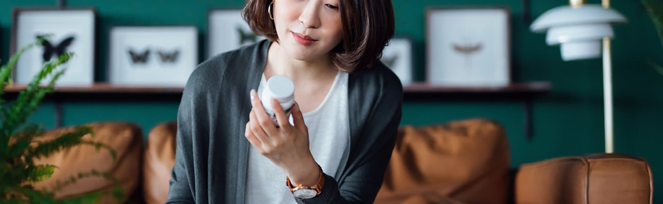 A young Asian woman in a well-decorated room looking contemplatively at the pill bottle