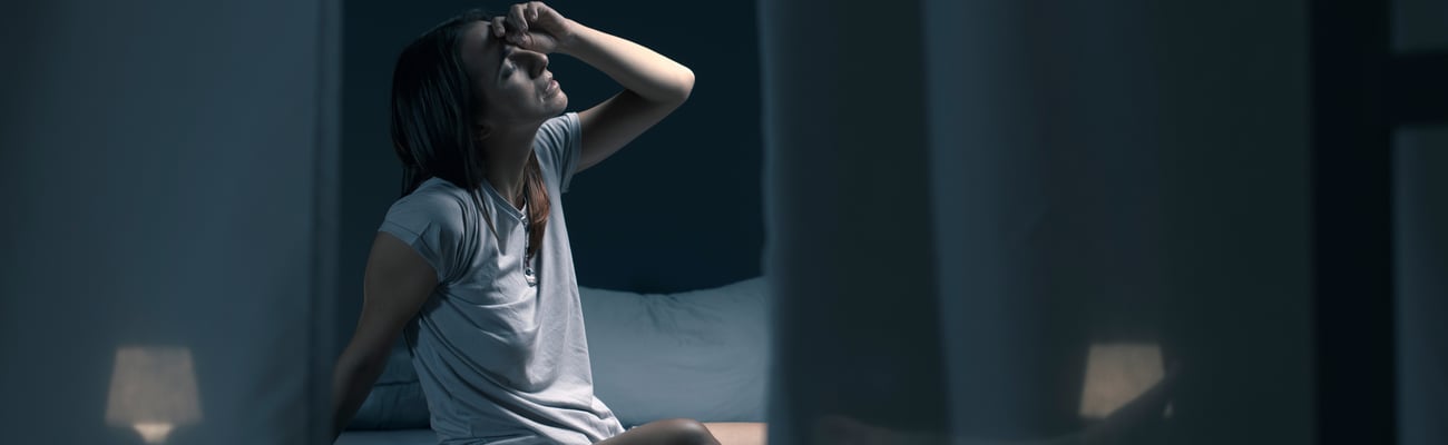 Young white woman on bed in darkened room holding head in distress, stress, hot, fatigue