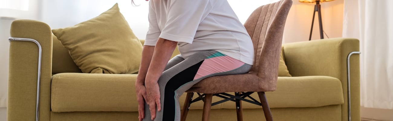 Older white woman doing chair yoga in her living room