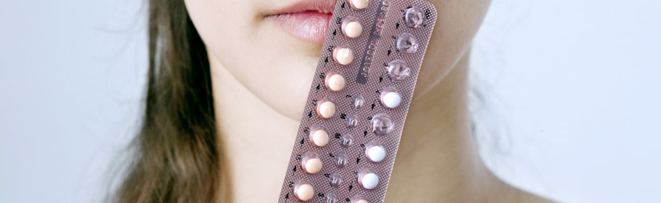 Young woman holding a packet of pills to her face