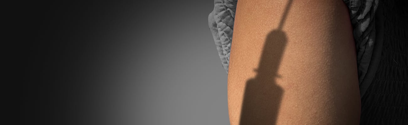 The shadow of a syringe looming over a woman's arm