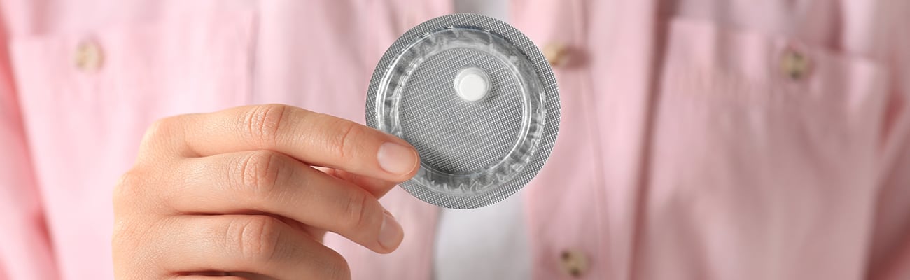 Woman holding a single wrapped emergency contraception pill