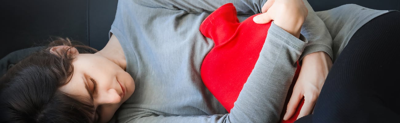 Teenager holding a hot water bottle to their stomach 