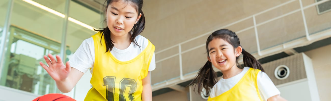 Two young Asian girls playing basketball with yellow jerseys
