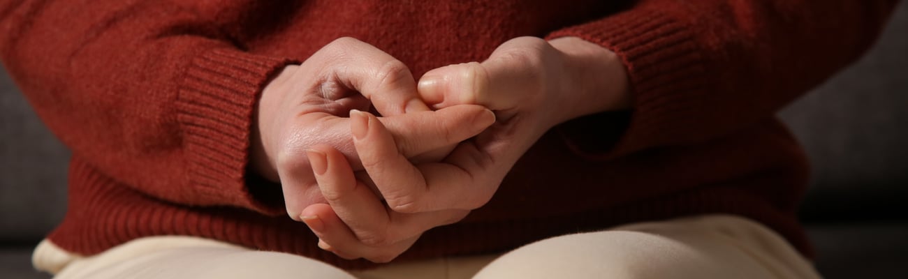 Close up of young adult clenching their hands and picking at the skin on their fingers