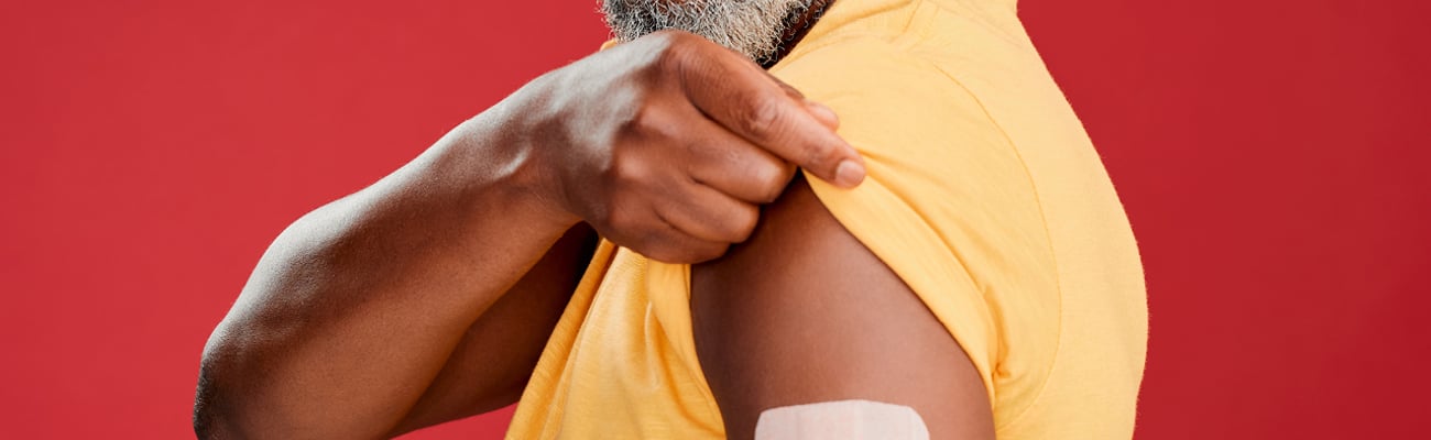 Middle-aged Black man holding up his yellow sleeve to show off a bandage where he received a vaccination