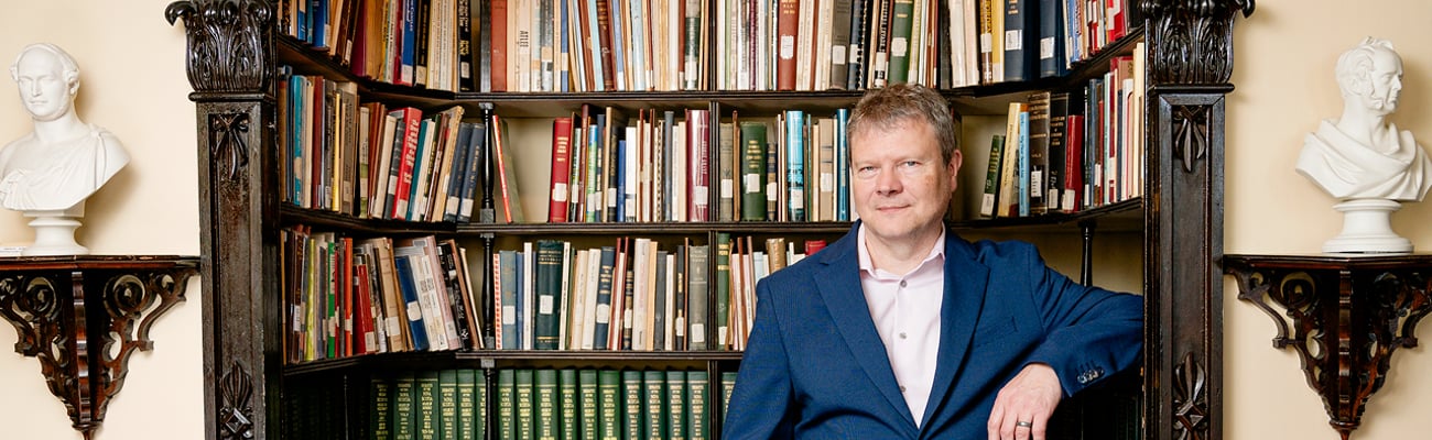 Graham MacKenzie standing in front of a sprawling bookshelf 