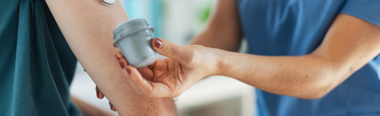 A woman with a continuous glucose monitor in her arm and a pharmacist helping her with it