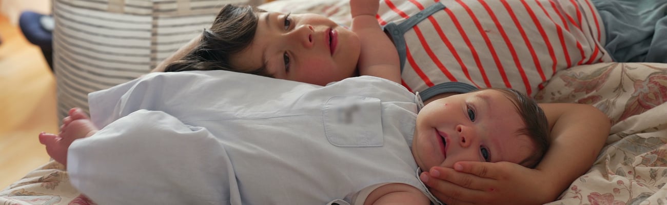 little white boy and white baby lying on bed together, boy cradling baby's head