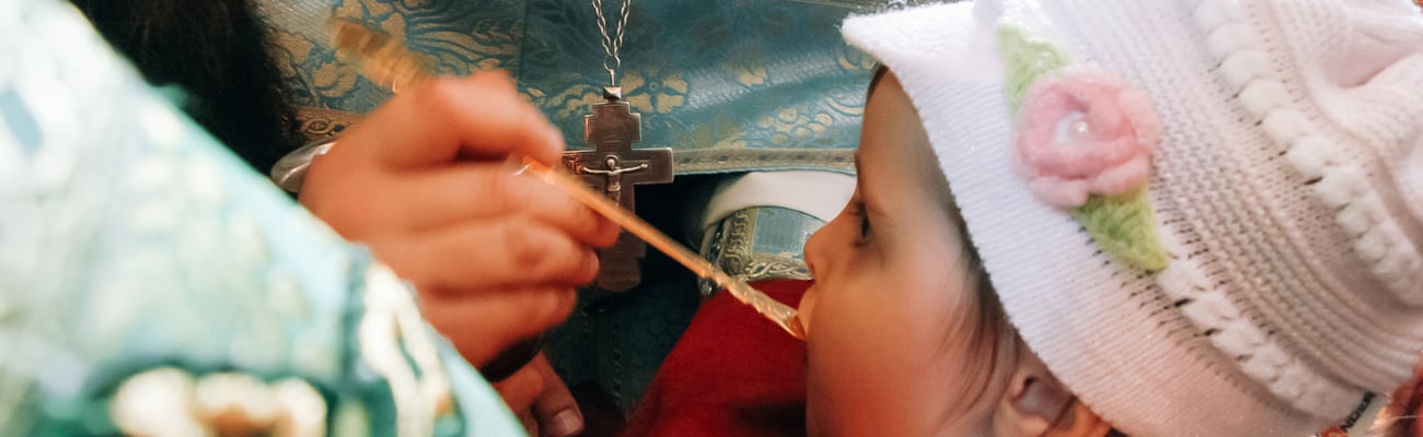 A child receives communion using a shared communion spoon at an Orthodox church.