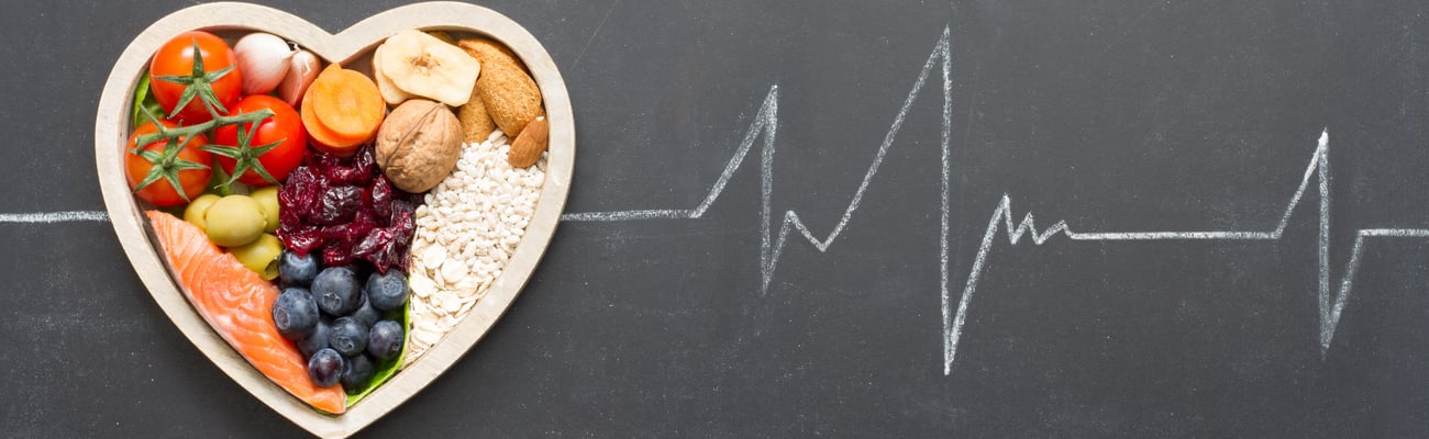 heart-shaped bowl of healthy produce on backdrop of heartbeat ECG graph.