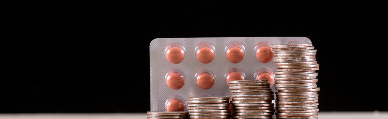 A stack of coins in front of a pack of pills