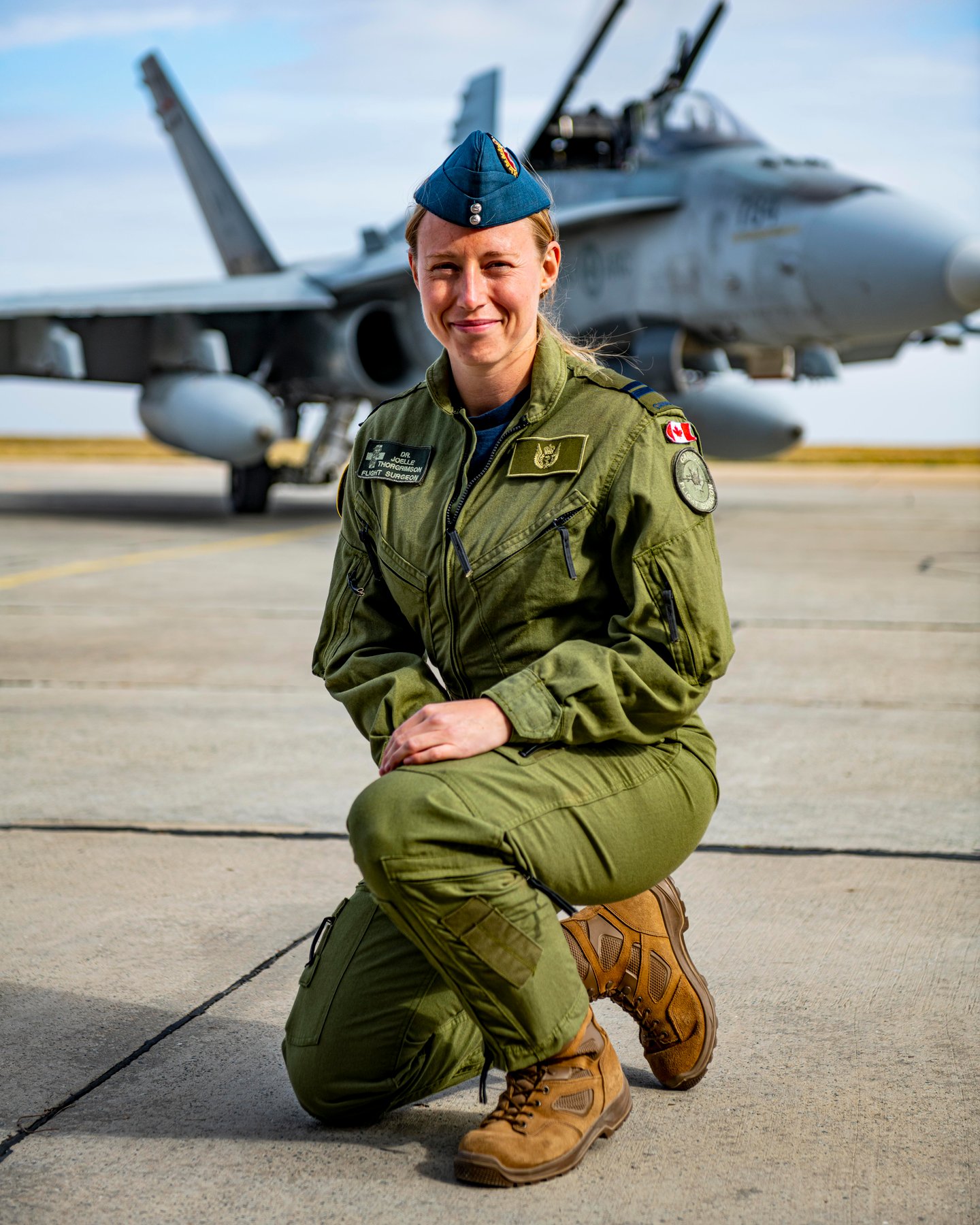 Dr. Thorngrimson crouched on tarmac, in khaki uniform, helicopter in background