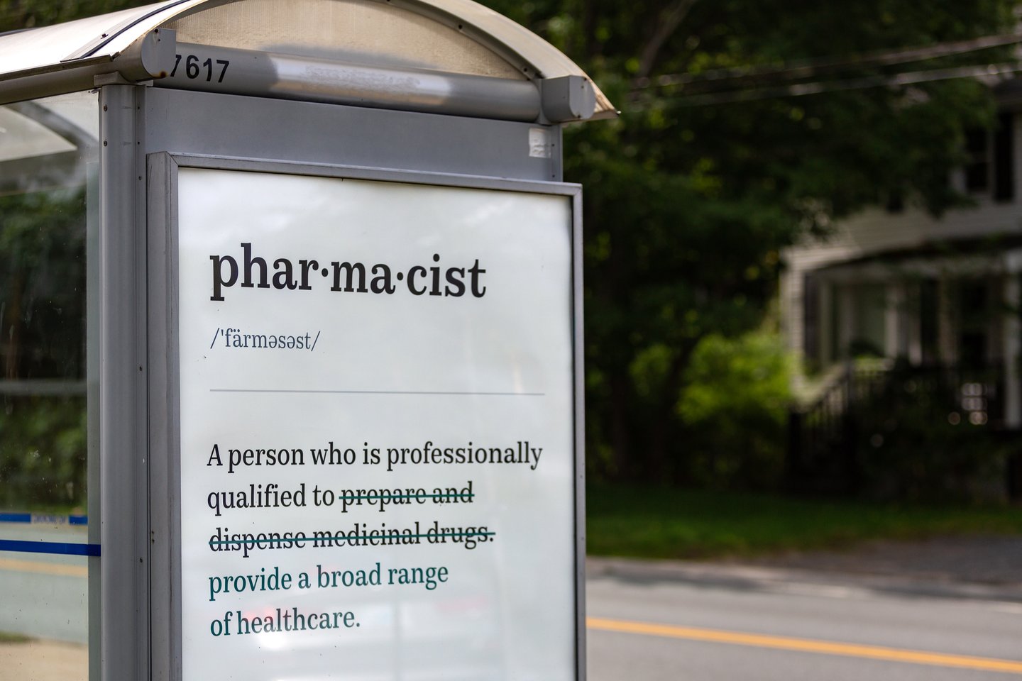A bus stop with an ad with the new definition of "pharmacist"