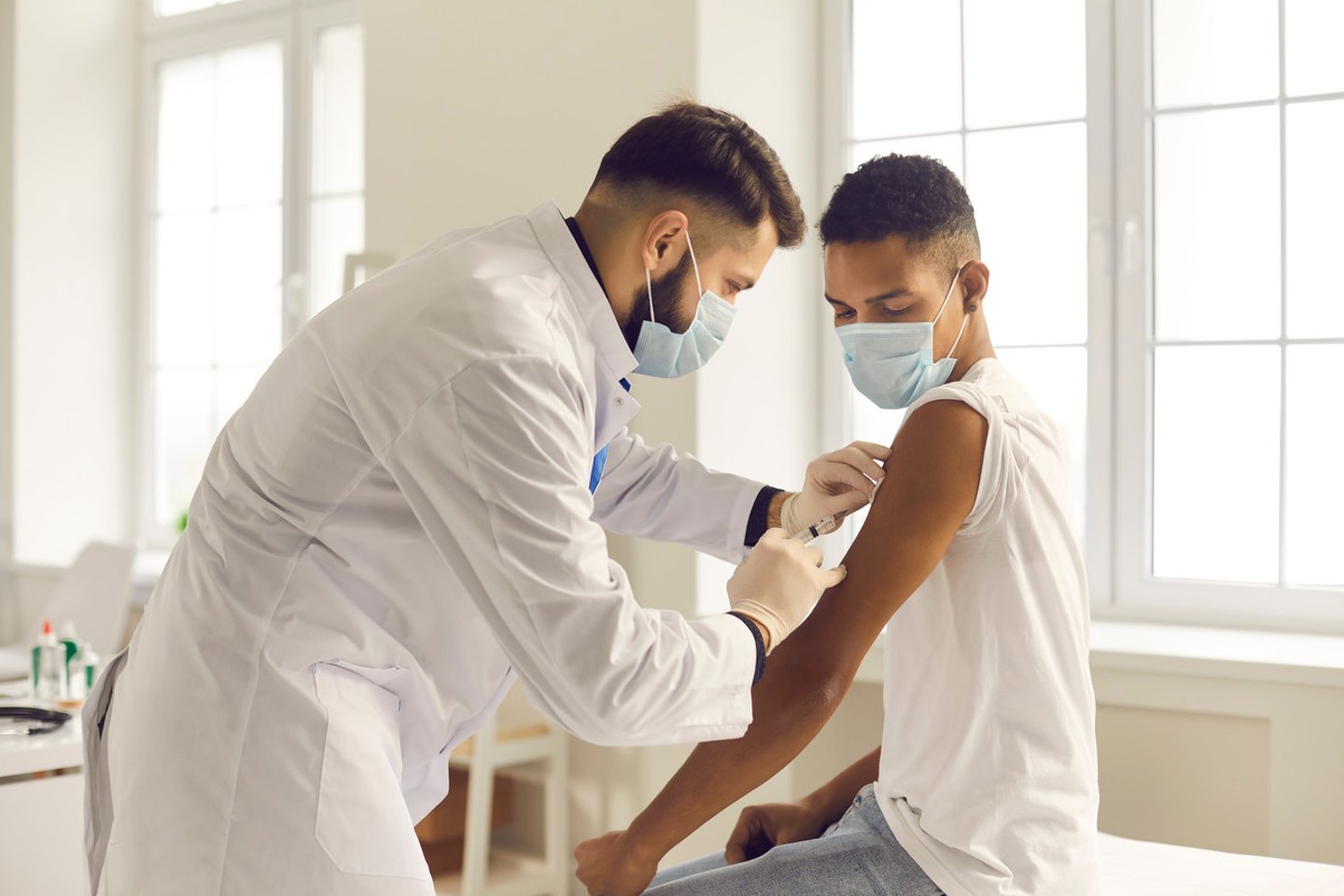 Doctor in medical face mask giving injection to patient during vaccination campaign at the clinic. Young African-American man getting Covid-19, AIDS or flu antivirus vaccine shot at the hospital; Shutterstock ID 1874064979